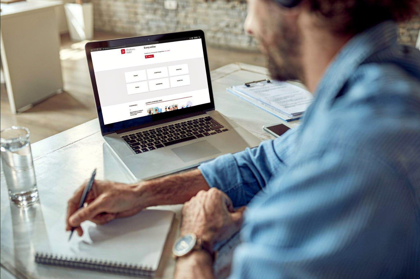 Mężczyzna siedzi przed komputerem, a na ekranie strona Akademii PARP